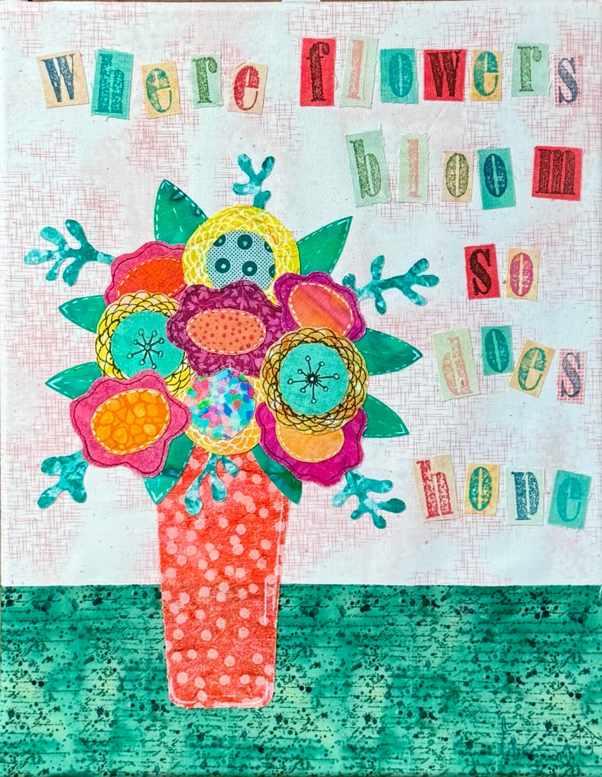A fabric collage of a bright bouquet in an orange polka-dot vase, with the words where flowers bloom so does hope spelled in fabric letters
