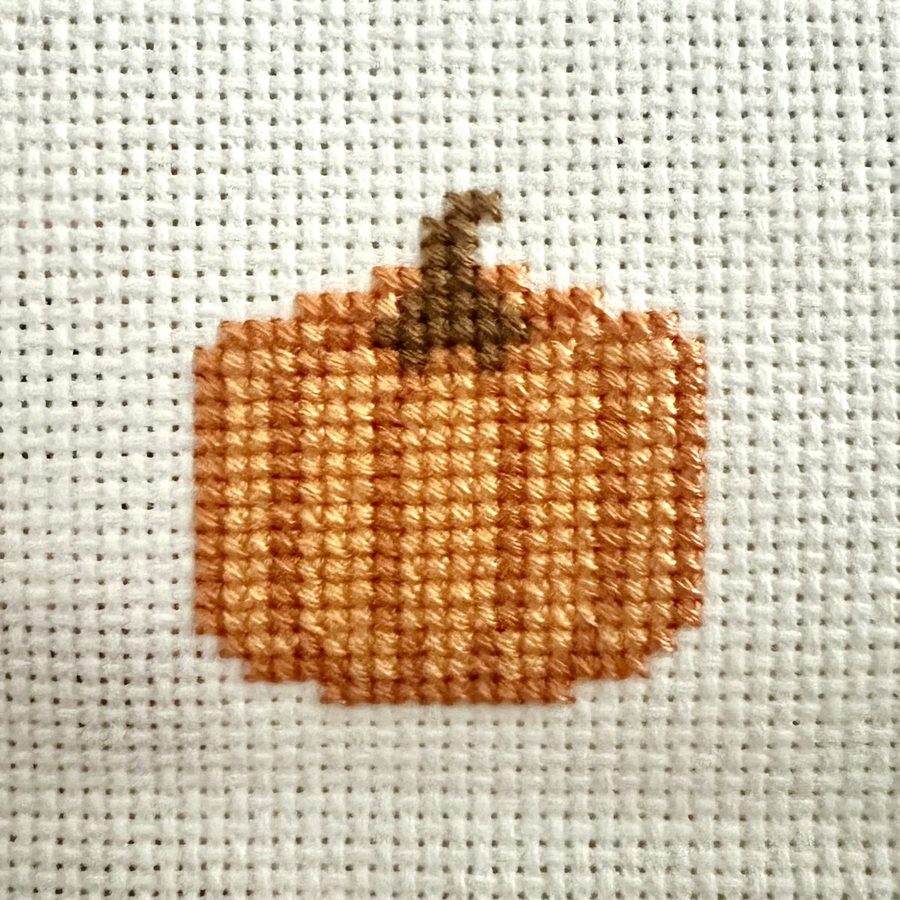 A small cross-stitched orange pumpkin worked on white aida cloth